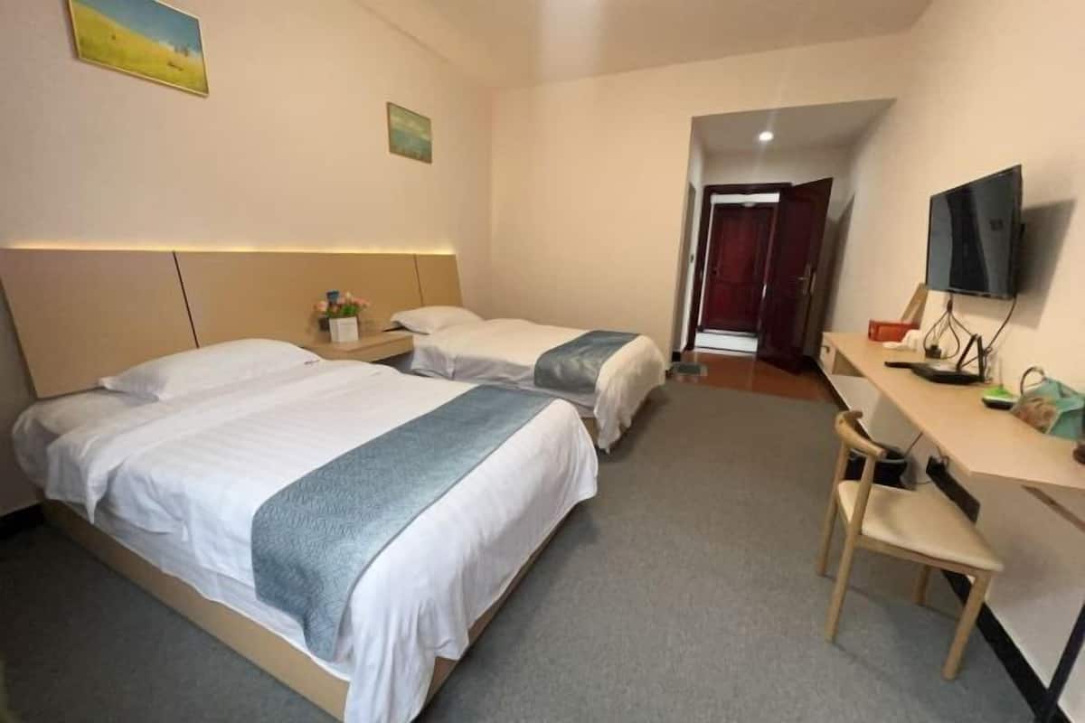 Une chambre d’hôtel avec deux lits, un bureau, une chaise, une télévision et une porte donnant sur une autre pièce.