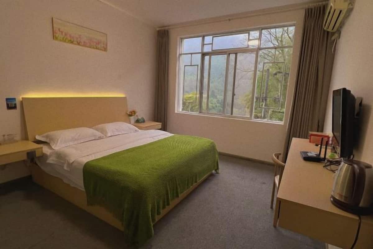 Une chambre d’hôtel équipée d’un lit, d’un bureau, d’une chaise, d’une fenêtre avec des rideaux et d’un climatiseur fixé au mur.