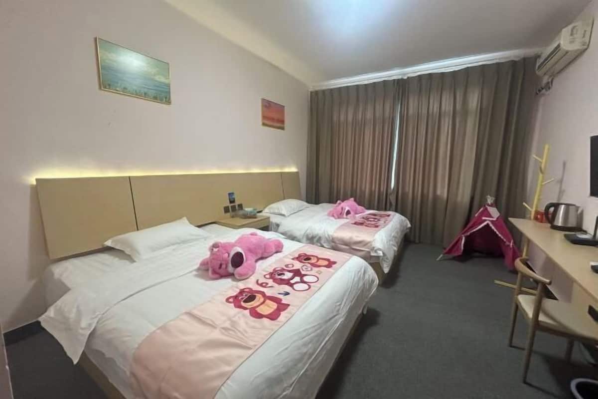 Une chambre d’hôtel avec deux lits, un bureau, une chaise, une petite table, un ours en peluche et une tente.