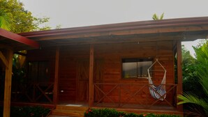 Una cabaña de madera con un porche, una hamaca y un pequeño jardín con flores rojas.