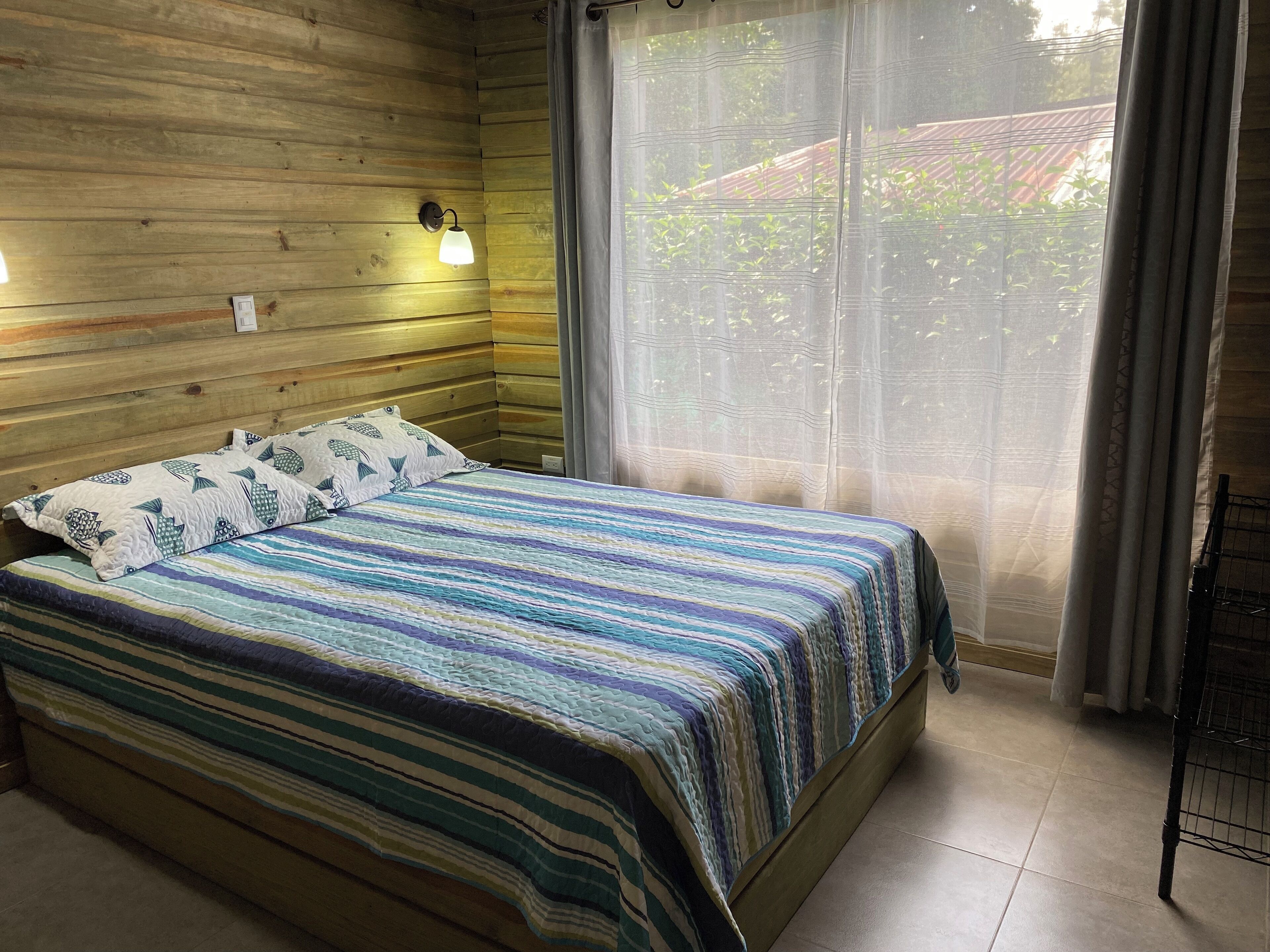 Ein Zimmer einer Holzblockhütte mit einem Bett, einer Wandleuchte und einem Fenster mit Vorhängen.