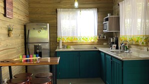 Una cocina con armarios color turquesa, un refrigerador, un lavamanos y un comedor con taburetes.