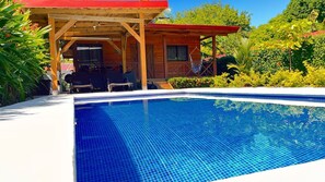 A swimming pool with a wooden deck and a covered seating area. - Cabaña Valfio Bahía Ballena (Uvita)