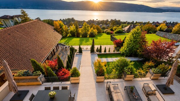 A rooftop terrace with a view of a lake, a well-maintained lawn, and a dining area with tables and chairs.