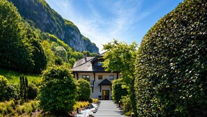 A pathway leading to a building surrounded by greenery and a mountain backdrop.