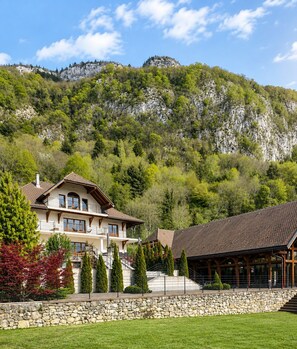 A two-story building with a balcony, surrounded by a stone wall and a grassy area.