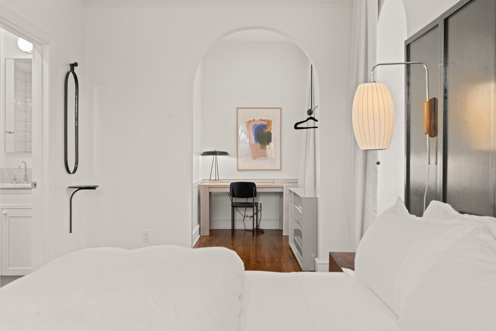 Un dormitorio moderno y minimalista con una cama grande, un escritorio con silla y una zona de ducha.