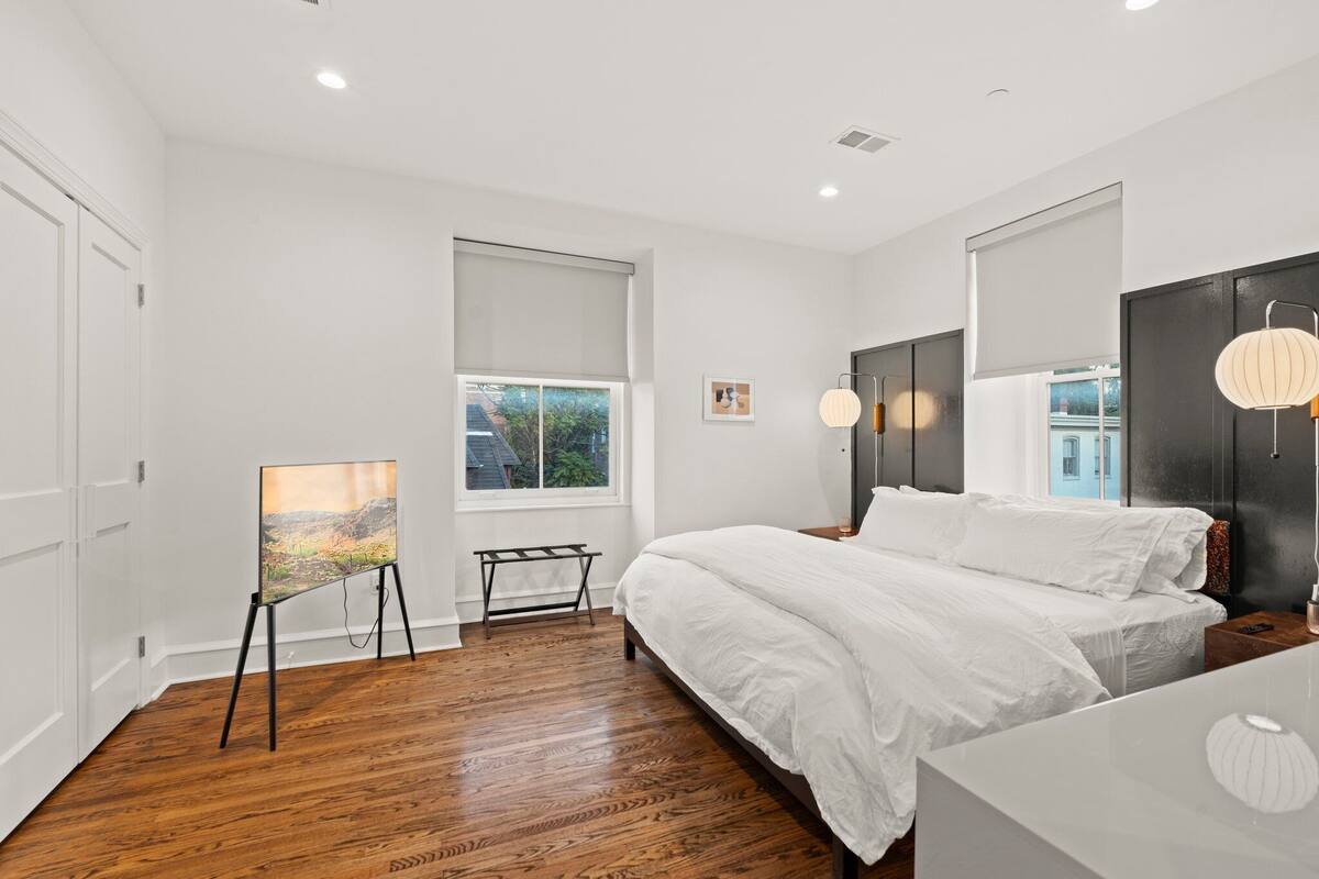 A modern bedroom with a large bed, a standing desk, and a painting on an easel.