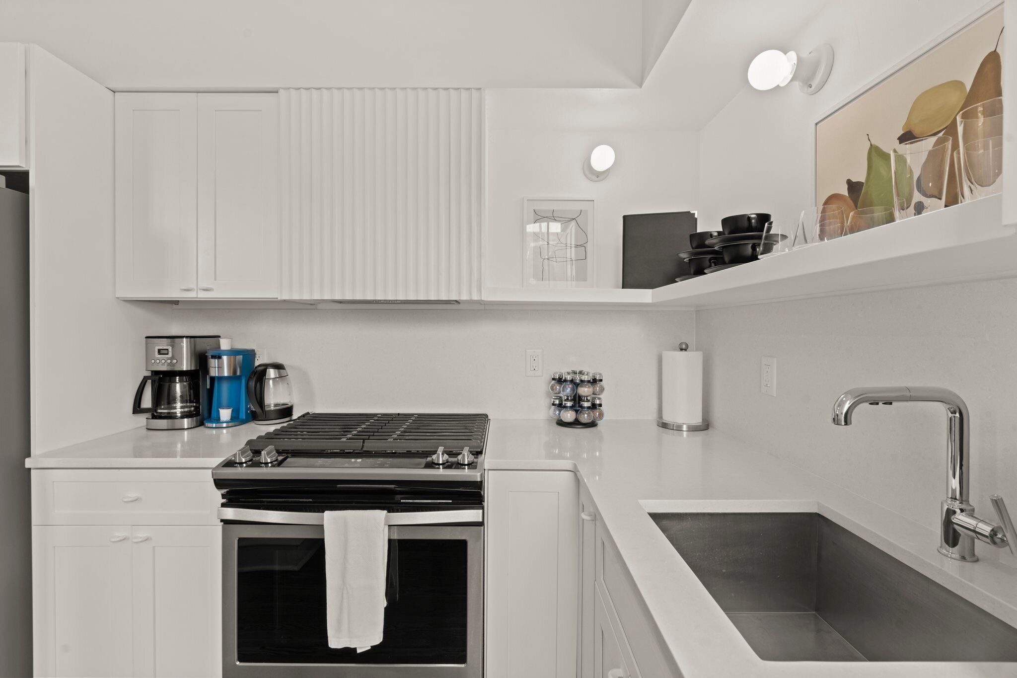 Een moderne keuken met witte kasten, een ingebouwde oven, een koffiezetapparaat en een roestvrijstalen spoelbak.