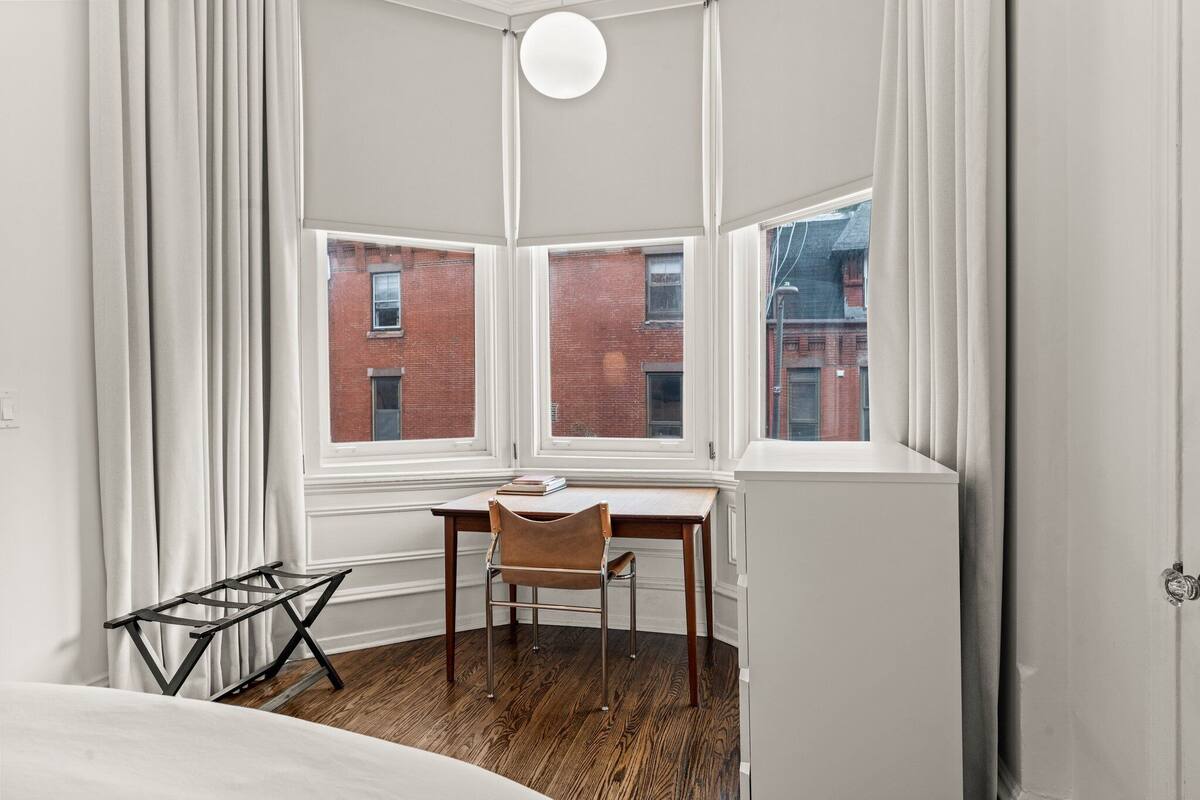 A corner room with a wooden desk, a chair, and a window overlooking a brick building.