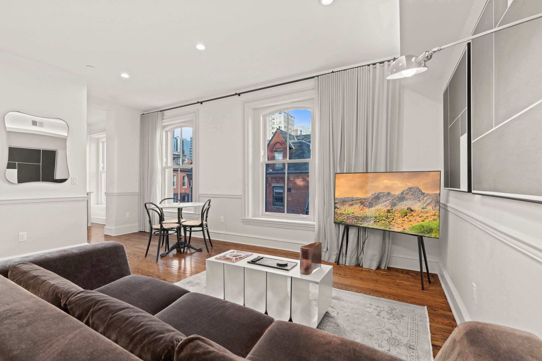 Una sala de estar moderna con un televisor de pantalla plana grande, un comedor con mesa y sillas, y ventanas amplias con vista a la ciudad.