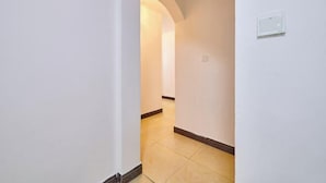 Een smalle gang met witte wanden en een betegelde vloer, die leidt naar een kamer met een zichtbare deur.