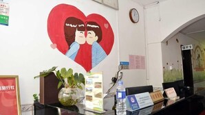 Een receptiebalie met een grote muurschildering van een hart, een klok, ingelijste certificaten en een bordje voor een kamer met extra services.