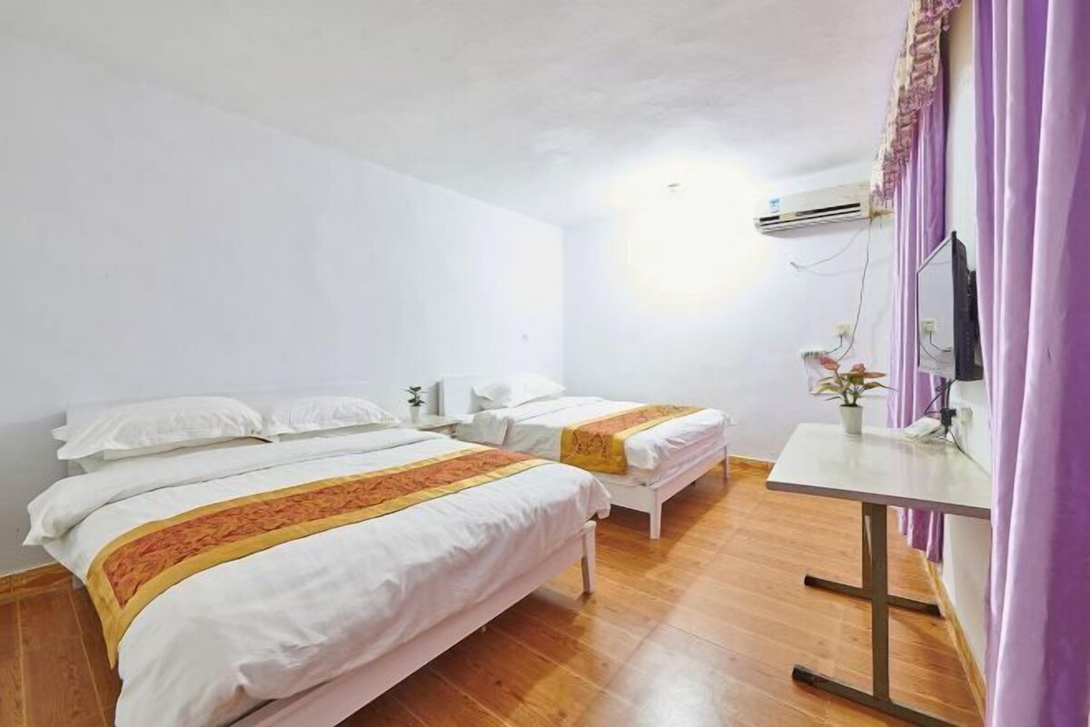 Een hotelkamer met twee bedden, een houten vloer, een klein tafeltje, een televisie en een wandairconditioner.