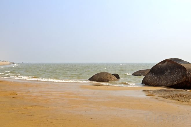 A beach with large rocks and calm water.