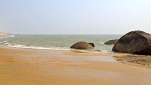 Een strand met grote rotsen en rustig water.