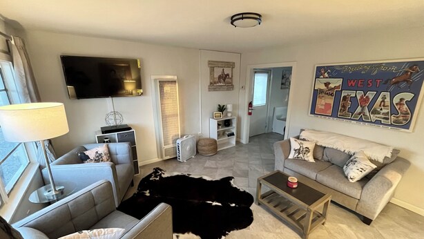 En moderne stue med sofa, sofabord og fjernsyn. Der er en ko i rummet, og et skilt på væggen med teksten "West Texas".