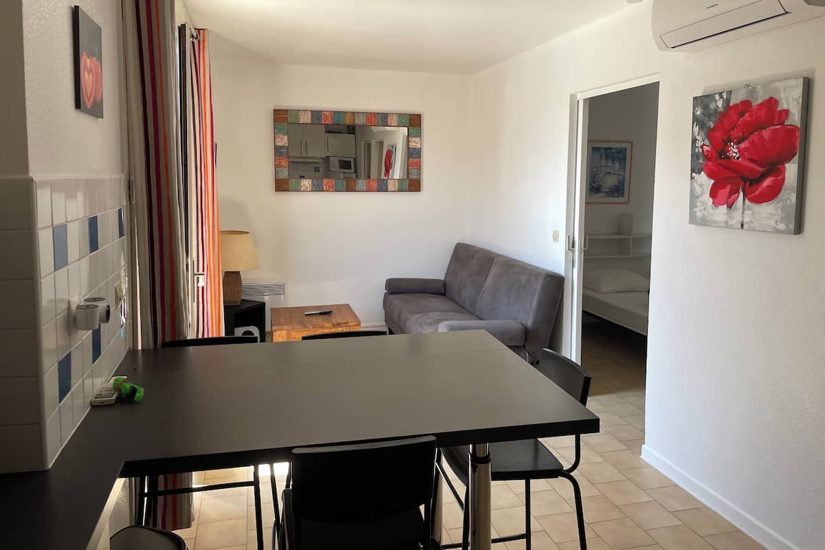 A compact living space with a kitchenette, a gray sofa, a small table, and a mirror.