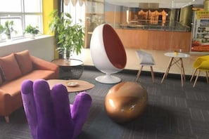 Un área de descanso moderna con un sofá, una silla huevo original, una mesa redonda y una butaca morada.