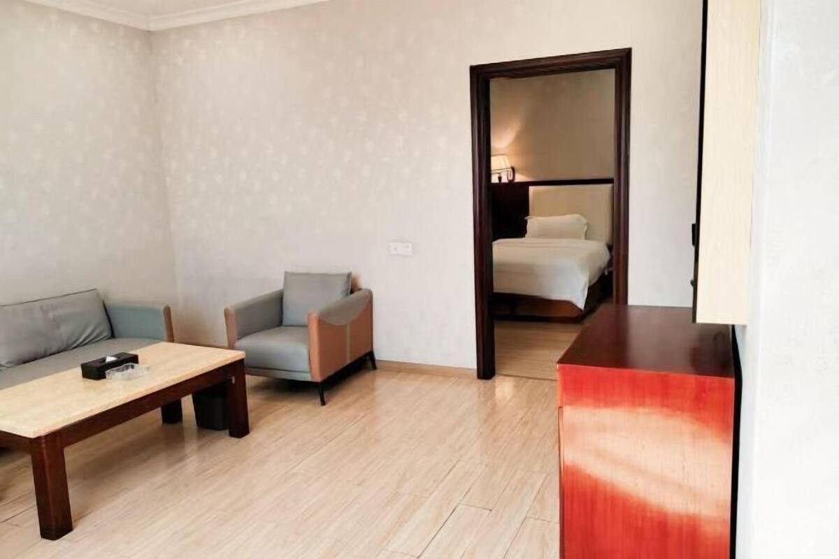 Une chambre d’hôtel équipée d’un canapé, d’un fauteuil, d’une table basse en bois et d’un lit avec une table de chevet.