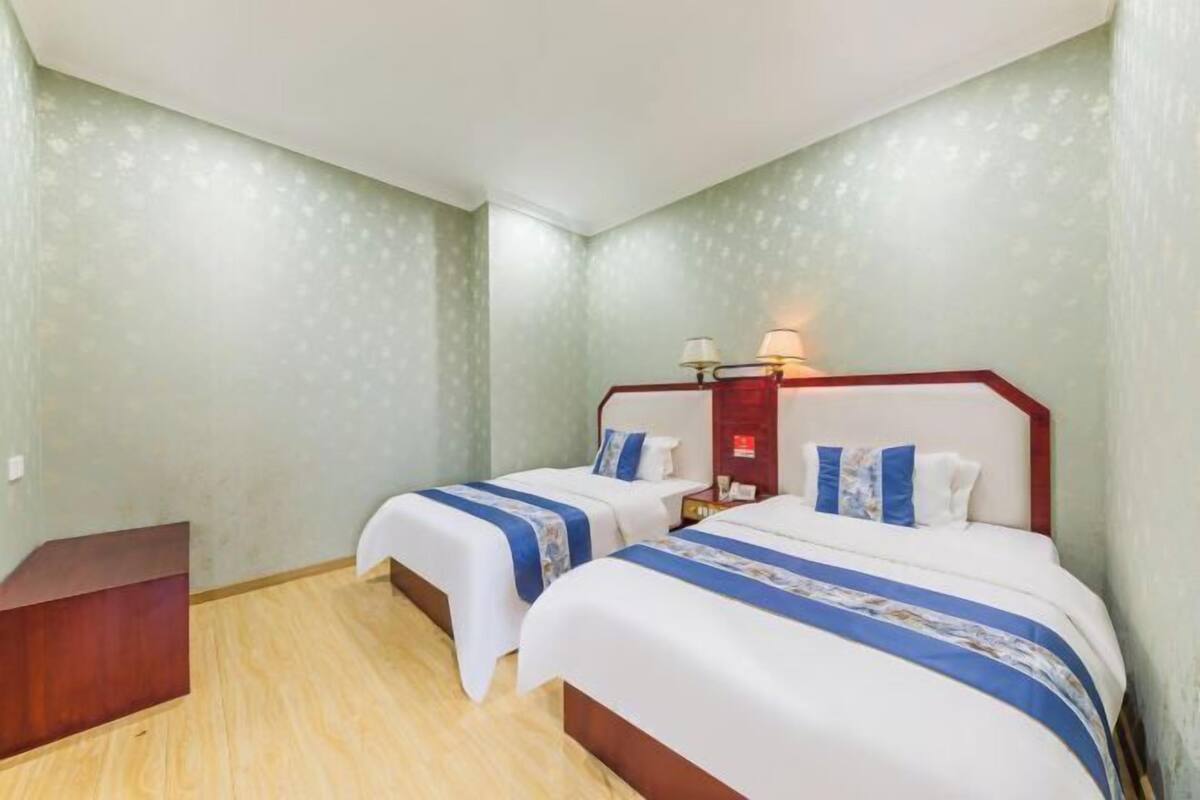 Une chambre d’hôtel avec deux lits, une table de chevet, un banc en bois et une lampe fixée au mur.