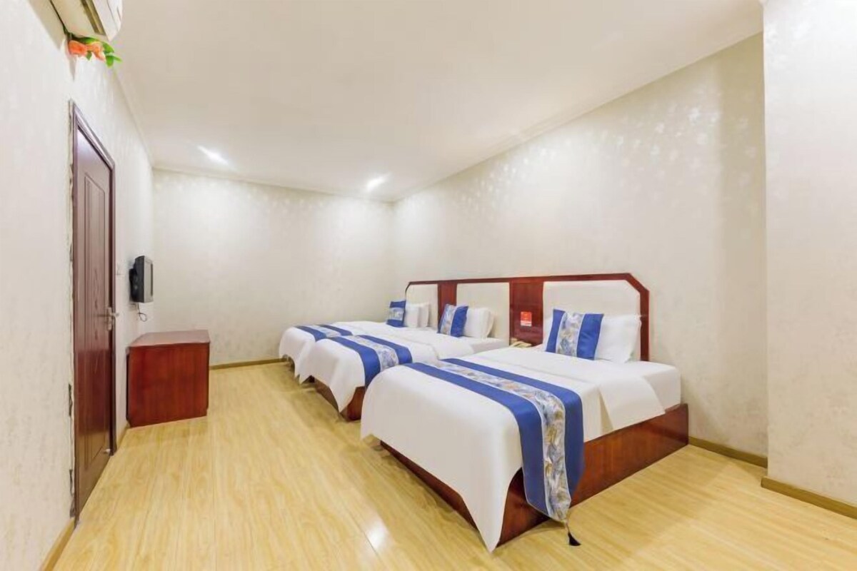 Ein Hotelzimmer mit zwei Betten, einem hölzernen Kopfteil, einem kleinen Nachttisch und einem an der Wand montierten Fernseher.