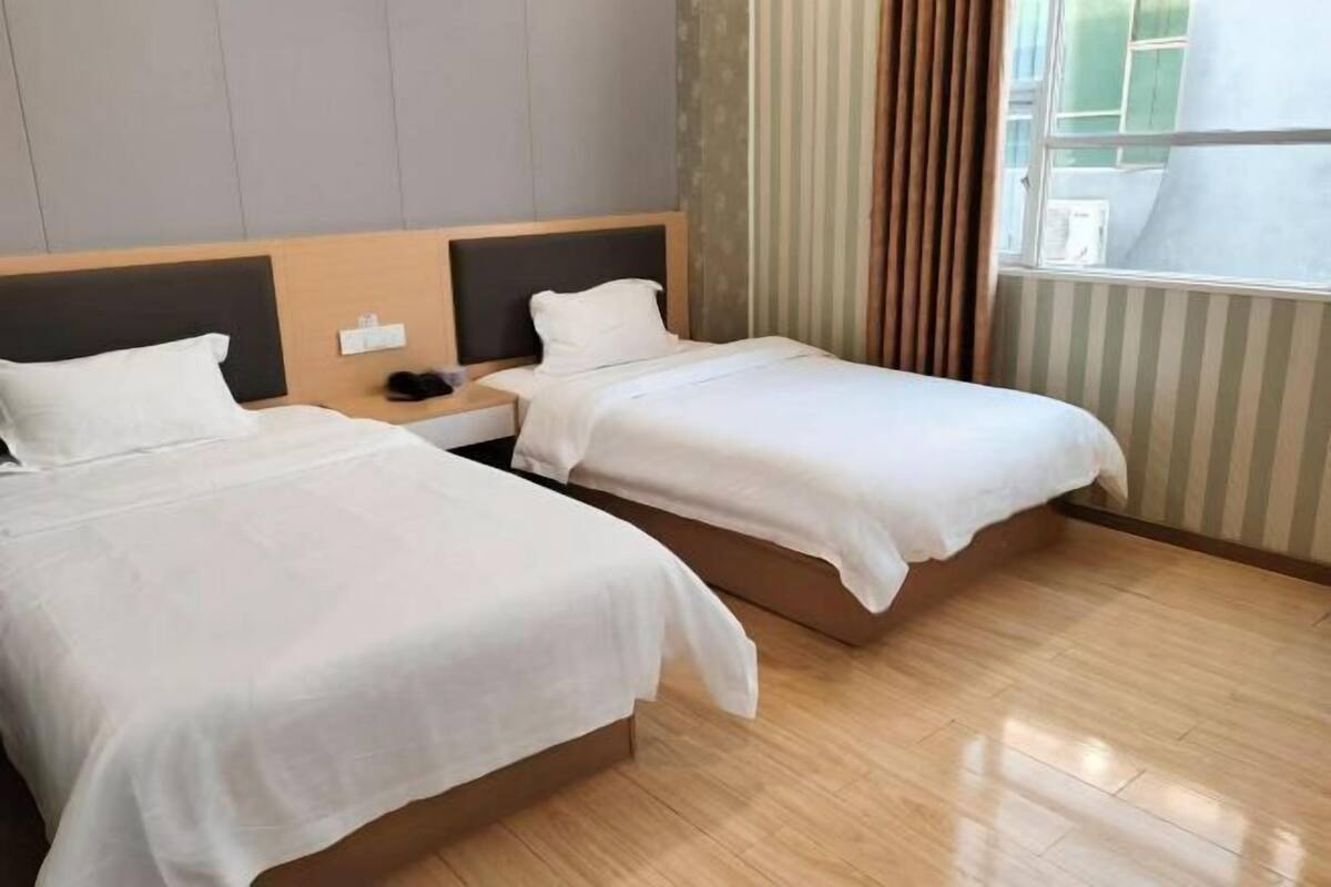 Une chambre d’hôtel avec deux lits, une table de chevet, une fenêtre avec des rideaux et un plancher en bois.