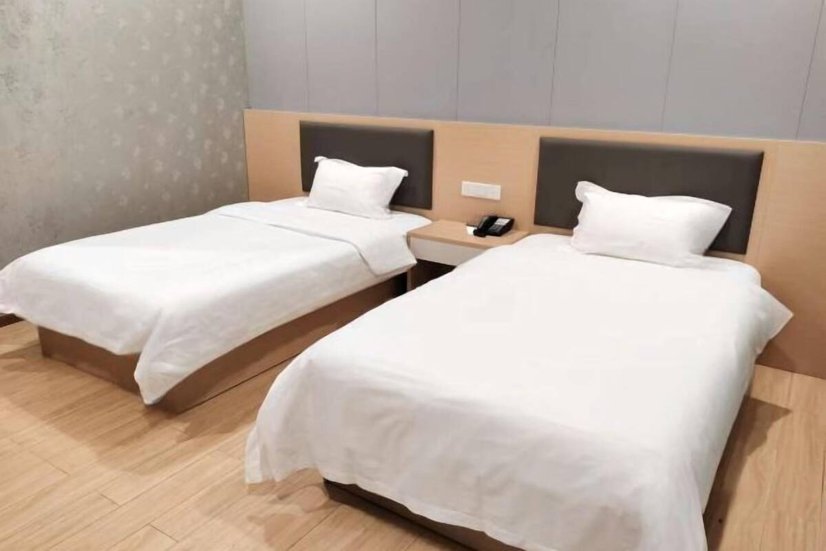 Deux lits simples avec des têtes de lit en bois et du linge de lit blanc, dans une chambre d’hôtel.