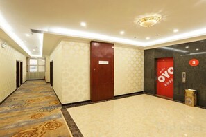 Un pasillo de hotel con alfombra estampada, una puerta de madera, una puerta roja con un letrero y un basurero fijado a la pared.