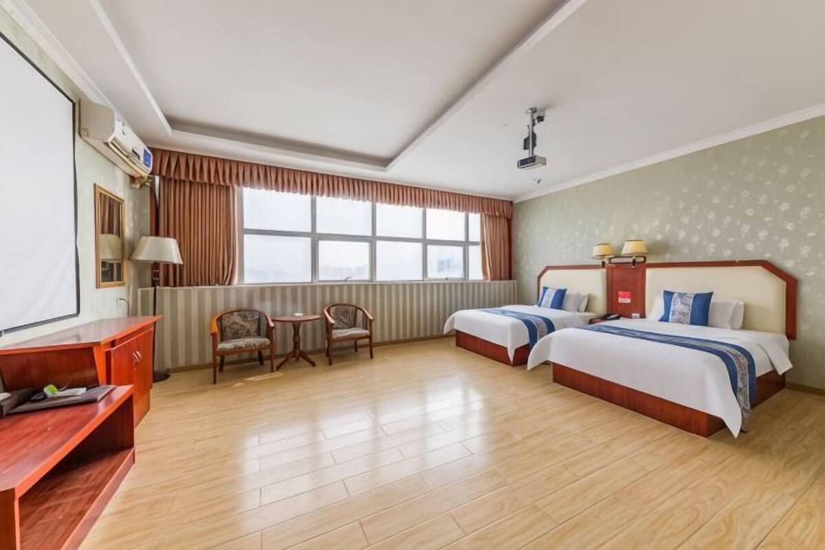 Une chambre d’hôtel avec deux lits, un bureau, une chaise, une fenêtre et un radiateur.