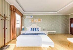 Ein Hotelzimmer mit Bett, Nachttischen, einer Lampe, einem Kleiderhaken und einem Fenster mit Vorhängen.