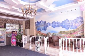 Un hall d’hôtel orné d’une fresque représentant une montagne, doté d’un lustre et comprenant un espace de réception avec un comptoir et des étagères.