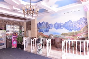 Un vestíbulo de hotel con un mural de montaña, un candelabro y una zona de recepción con mostrador y estanterías.