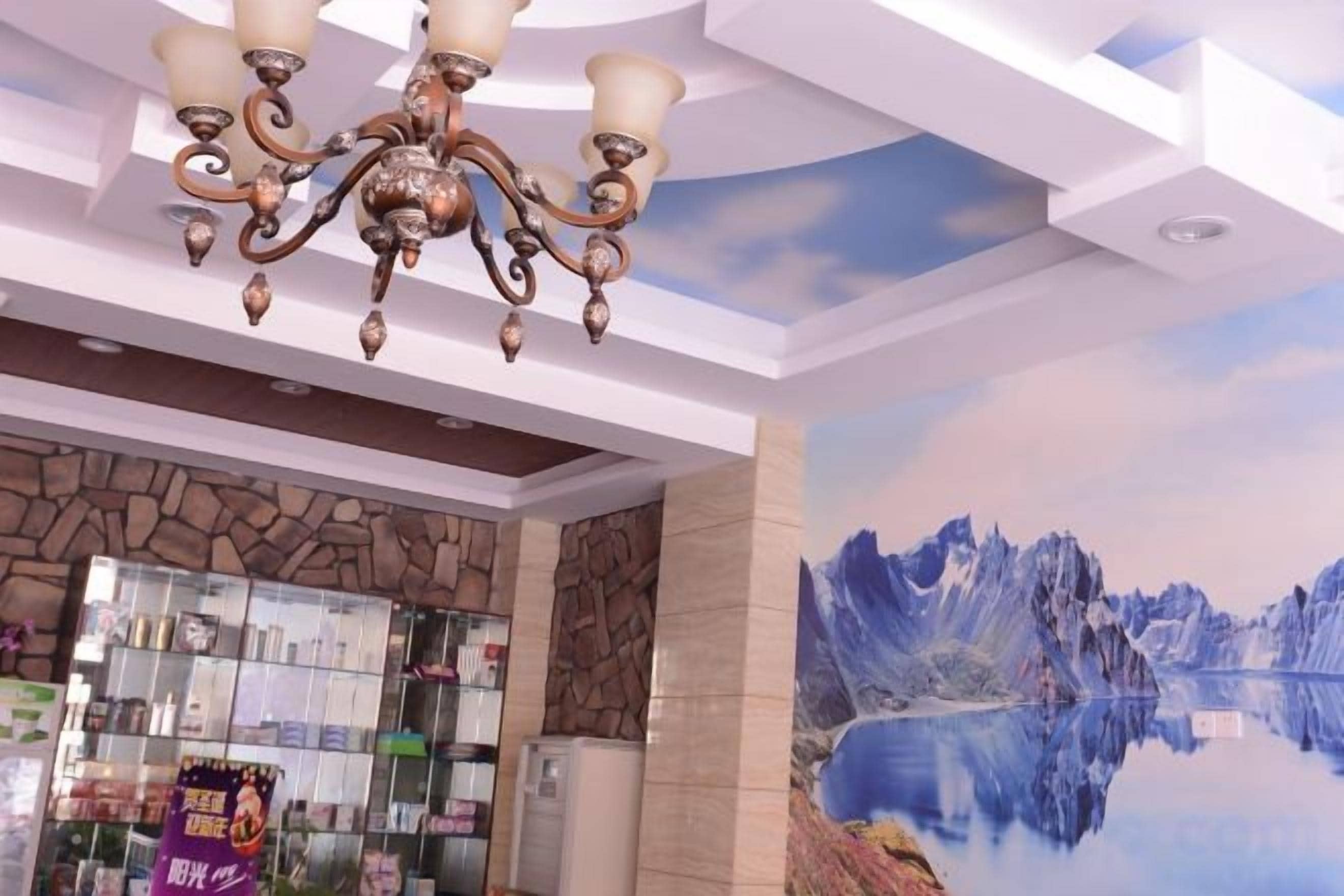 Vestíbulo de hotel con candelabro, pared de piedra, vitrina de cristal y un mural de montañas.