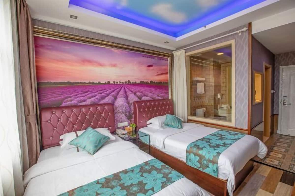 Une chambre d’hôtel avec deux lits, une grande fenêtre, un plafond avec un luminaire et une fresque représentant un champ de lavande.