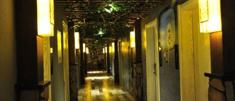 A hallway with a checkered floor, doors on either side, and wall-mounted lights.