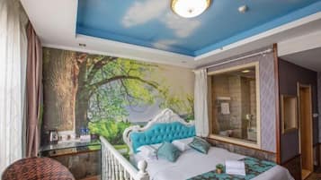 Una camera da letto con un grande affresco raffigurante una foresta, una testiera trapuntata, un letto con biancheria a motivi, una scrivania con una sedia e un bagno con box doccia in vetro.