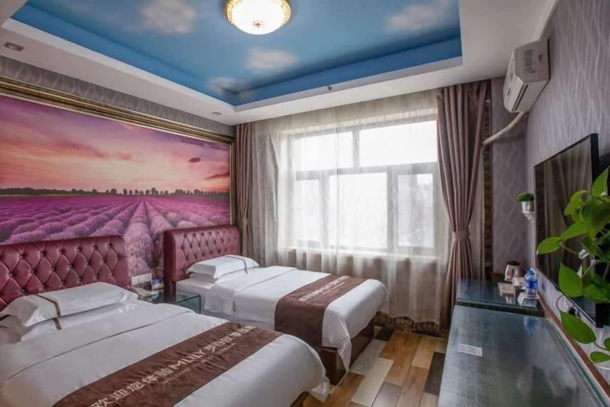 Une chambre d’hôtel avec deux lits, une grande fenêtre avec des rideaux, une fresque au plafond et un téléviseur fixé au mur.