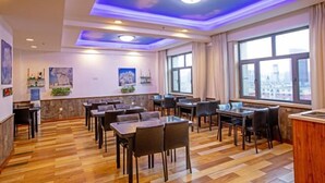 A hotel dining area with wooden flooring, tables, chairs, and large windows offering city views.