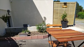 Un espace extérieur aménagé avec des tables et des bancs en bois, entouré d’une bordure en briques et agrémenté de plantes en pot.