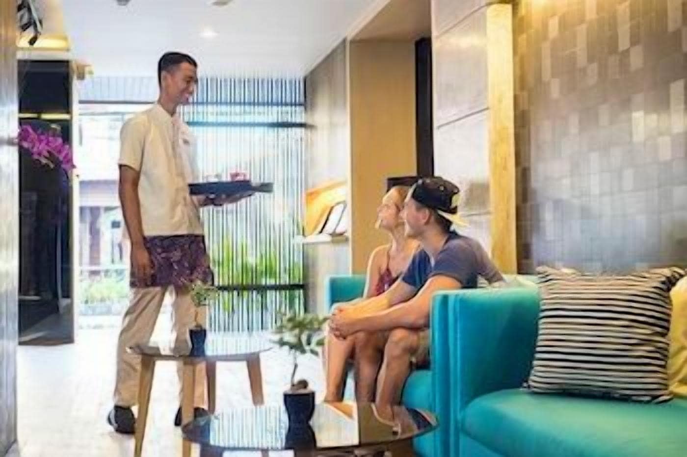 Un vestíbulo de hotel con una recepción, un área de estar con un sofá y sillones, y un ventanal con vistas.