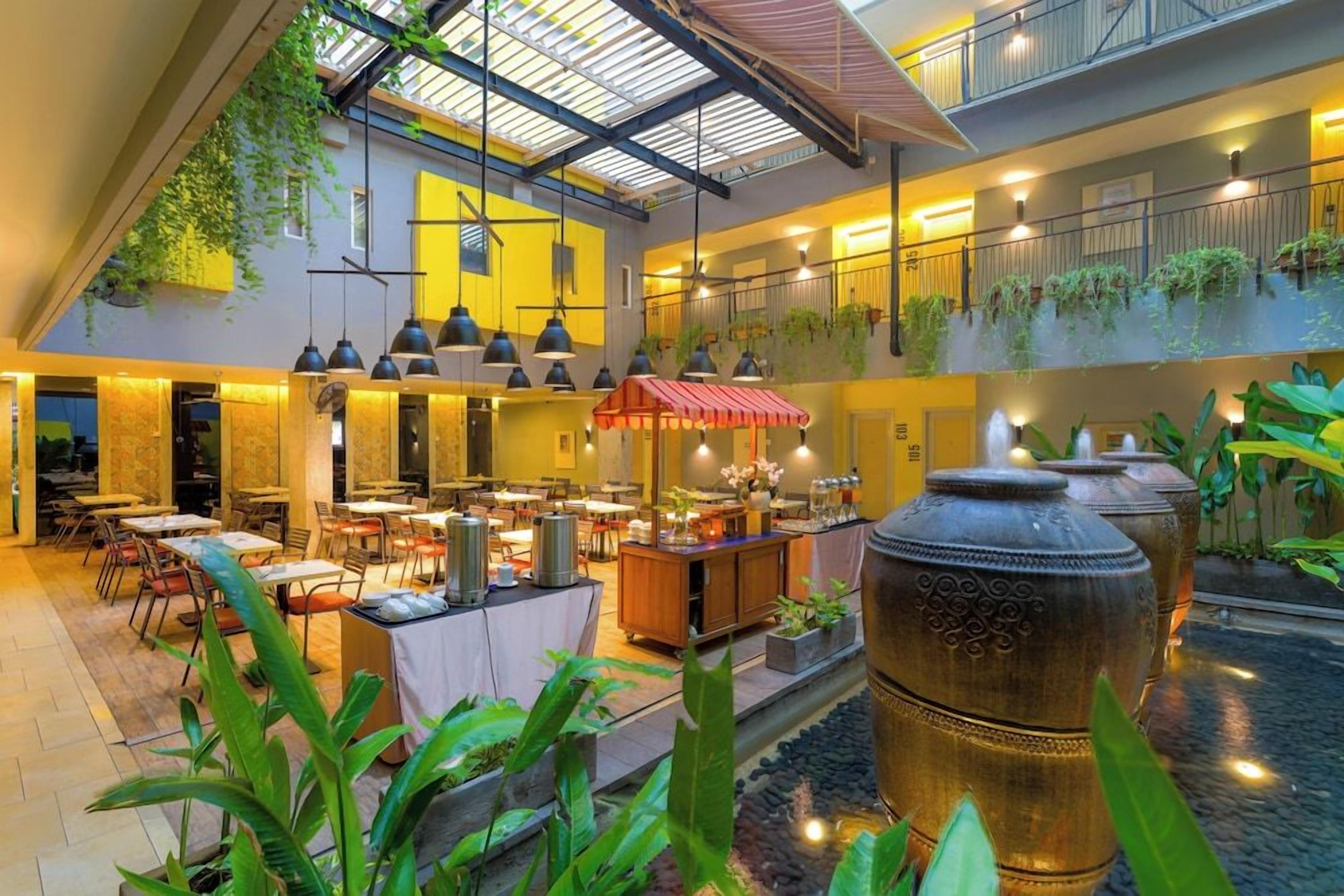 Amplio espacio interior con varias mesas y sillas para comer, una fuente central y plantas colgantes.