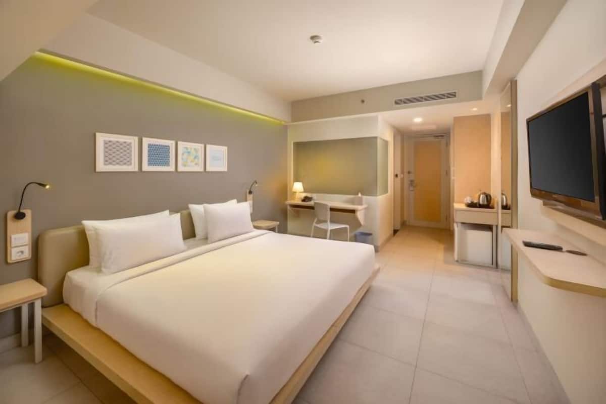 A hotel room with a bed, desk, chair, TV, and artwork on the wall.