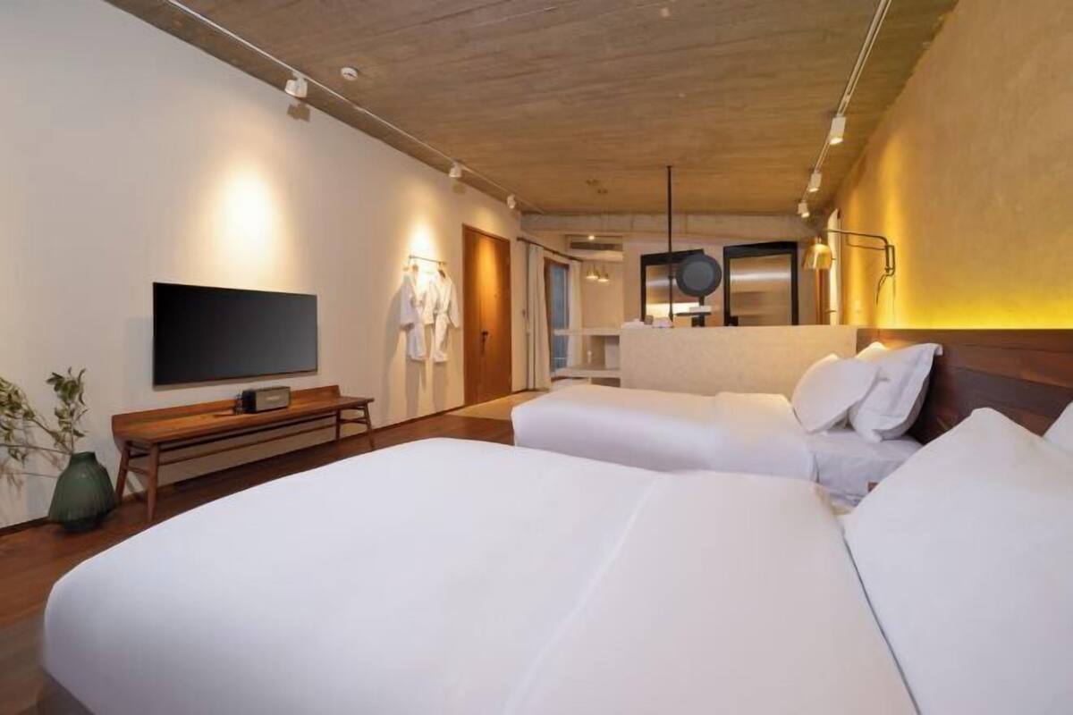 A hotel room with two beds, a TV, a bench, and a mirror.