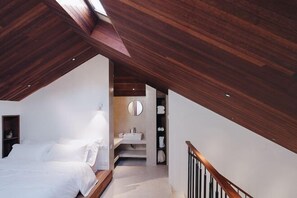 A bedroom with a sloped ceiling, a bed, a bedside table, a mirror, and a bathroom with a sink and towel rack. - Mount Mogan Chic Hostel (Deqing)