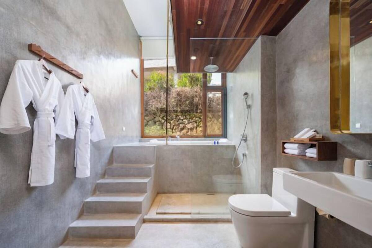 A modern bathroom with a large window, a walk-in shower, and a toilet.