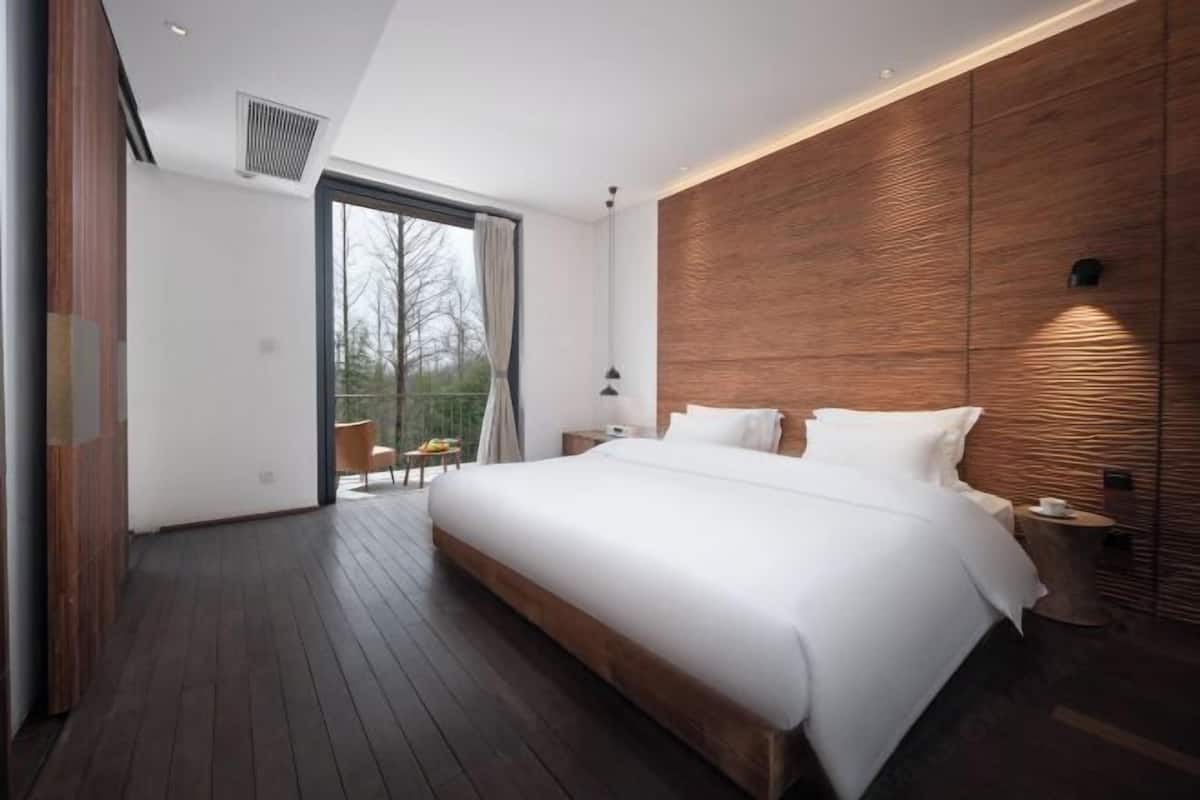 A modern bedroom with a large bed, wooden paneling on the walls, a small table, and a nightstand.