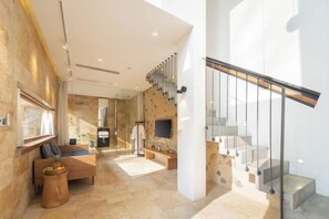 A spacious living area with a staircase, a sofa, a coffee table, and a stone wall. - Mount Mogan Chic Hostel (Deqing)