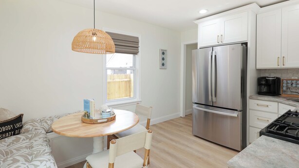 A modern kitchen with white cabinets, a stainless steel refrigerator, and a round wooden table with chairs. - Cozy 2-Bedroom Home: Modern Amenities, WiFi, and AC—3 Blocks from Pier Village (Long Branch)