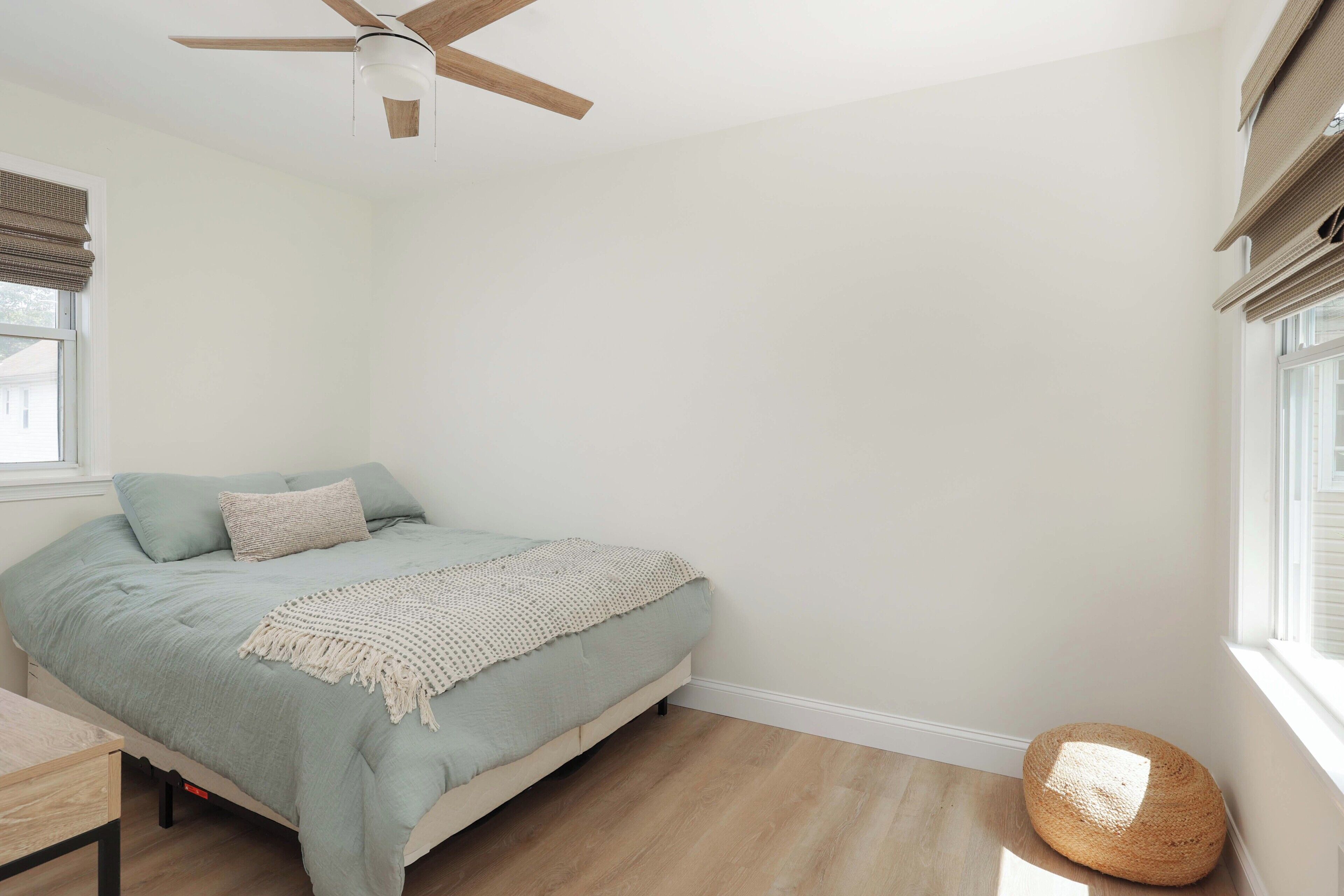 Une chambre à coucher avec un lit, un ventilateur de plafond, une fenêtre avec des stores et un plancher en bois.